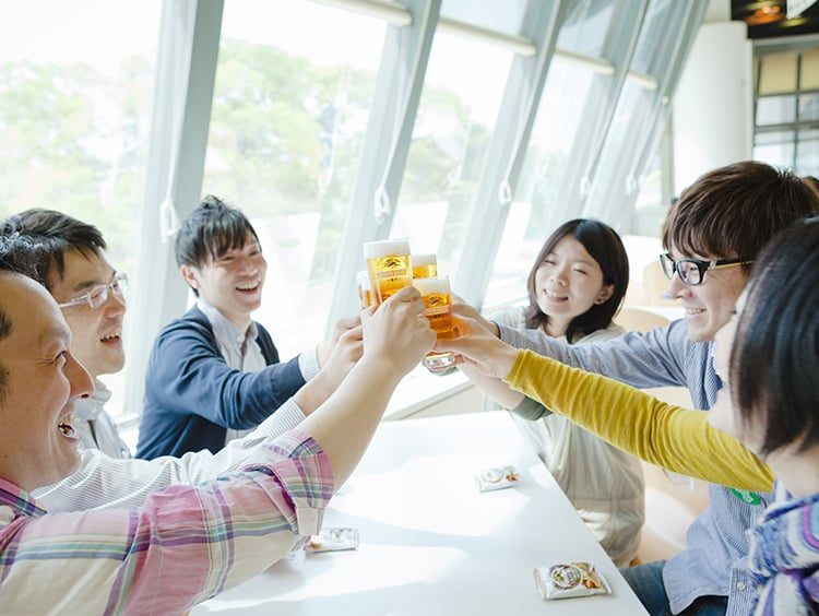 明るい部屋のカウンターで、参加者たちがビールの入ったグラスで乾杯している