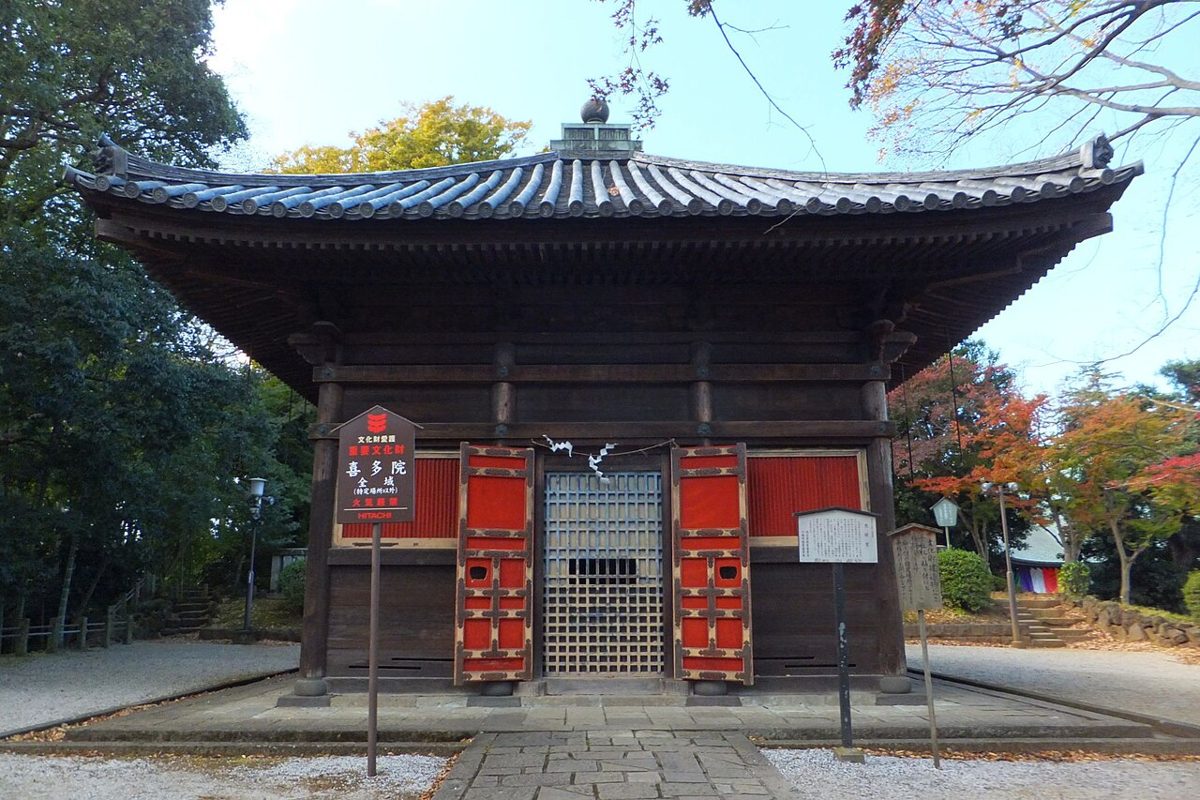 朱色の扉の木造のお堂「慈眼堂」と、右手奥の赤や橙に色づいた木々。手前に重要文化財を示す案内板