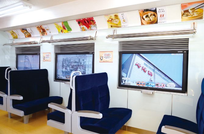 電車の座席のような青いシートが並び、窓の位置に崎陽軒の映像を映すタッチパネルの画面がある店内