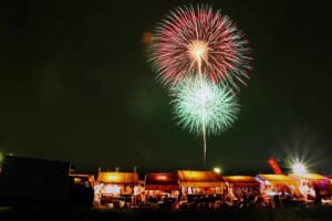 赤と緑の大輪の花火が夜空に開き、手前に屋台のテントが並ぶ小江戸川越花火大会の過去の様子