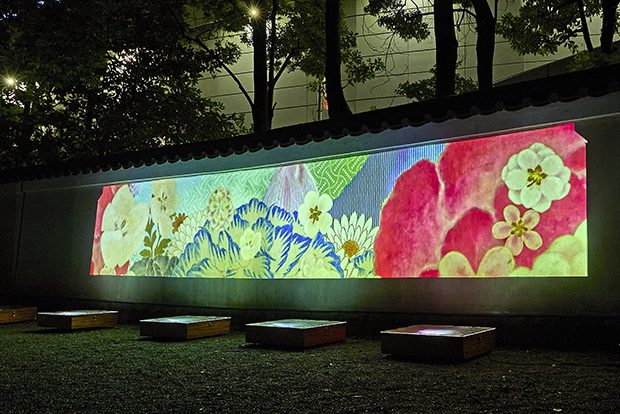 夜の庭で、瓦屋根の付いた塀に花や青海波の模様の映像が映し出されている