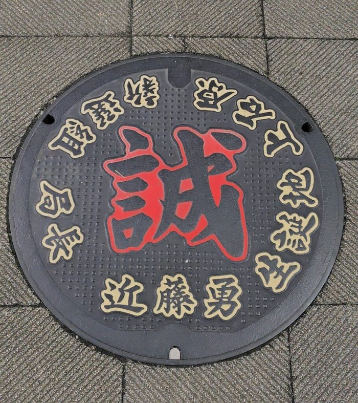 中央に赤い「誠」の字、周りに近藤勇の名が入ったマンホールの蓋