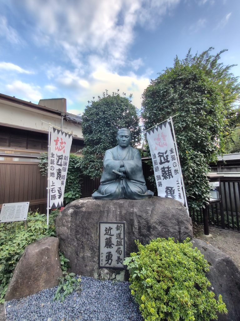 西光寺の門前にある、岩の上に座る近藤勇の銅像と「誠」の幟
