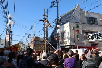 中山道で行われるはしごのり。はしごの上で演技する鳶職と、宮本町会の看板の前に集まる見物客