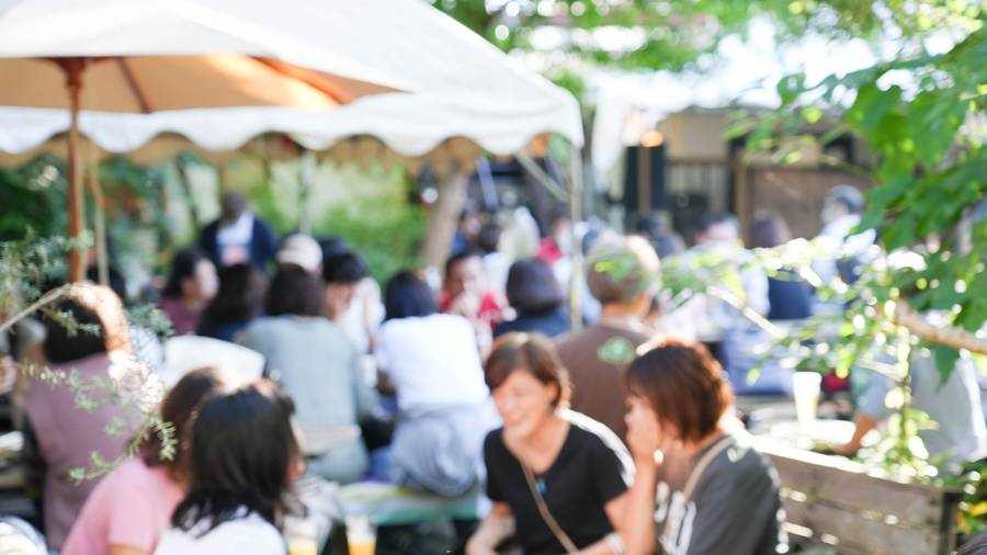 熊澤酒造オクトーバーフェストの庭。木々の下に白いパラソルが並び、テーブルを囲んだ来場者がビールを手に談笑している
