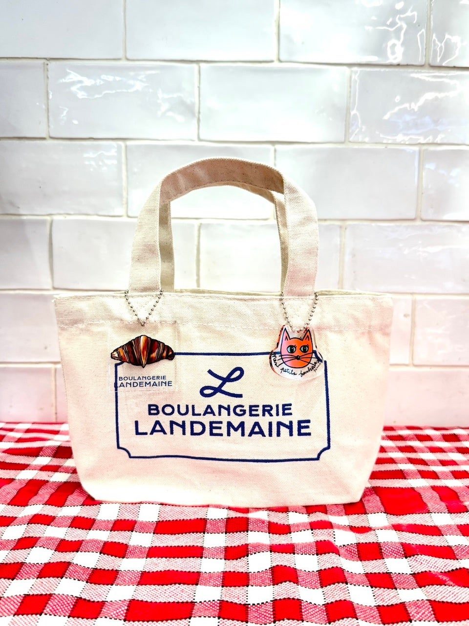 「BOULANGERIE LANDEMAINE」のロゴ入りミニトートバッグに、クロワッサンとオレンジ色の猫のチャームを付けた画像