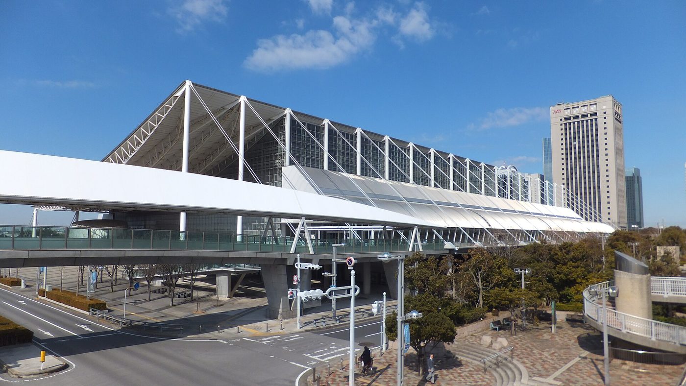 青空の下、白い柱とケーブルで支えた大屋根とガラス張りの壁が続く幕張メッセ国際展示場の9〜11ホールと、手前の歩行者デッキ