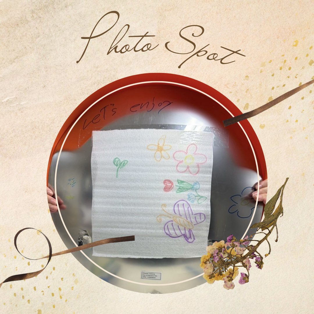 「Photo Spot」の文字と花の飾りに囲まれた丸い鏡に、花の絵を描いた紙が映っている