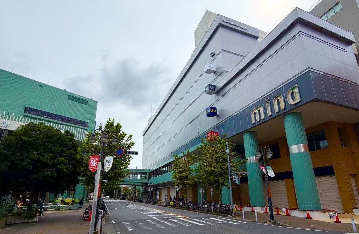 ミーナ津田沼の外観。灰色の外壁に「mina」のロゴと緑色の柱があり、ユニクロとGUの看板が掲げられた建物の前を道路が通っている