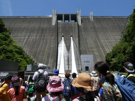 帽子をかぶった子どもたちの見学者越しに、ダムの正面から2本の放流を見る写真