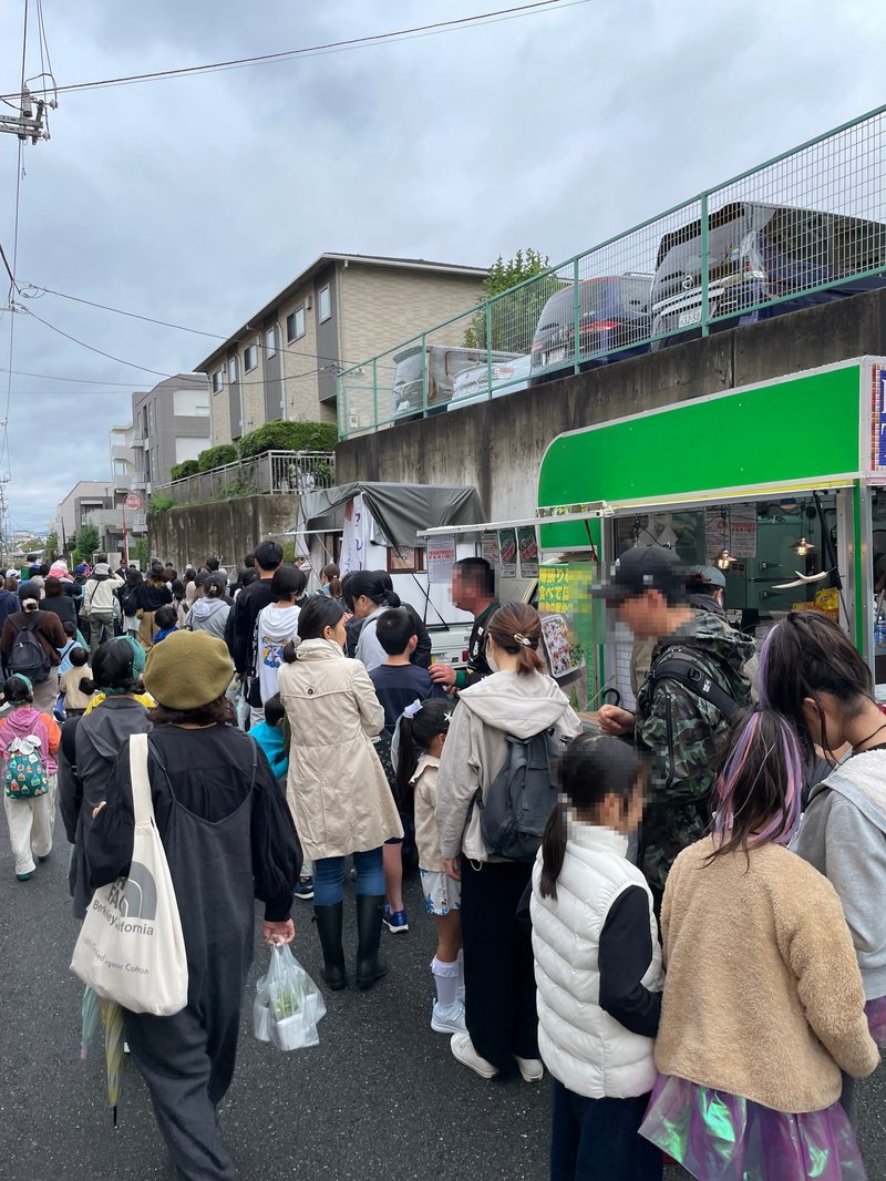 2023年の宮前区民祭。区役所周辺の道路に傘やリュックを持った来場者が列になって歩いている