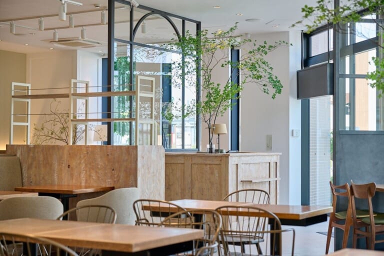 木のテーブルとソファ、枝ものを生けた花器があるSiKiTO CAFE幕張店の店内