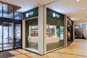 商業施設の通路に面した、緑の看板の小さなカフェの店頭