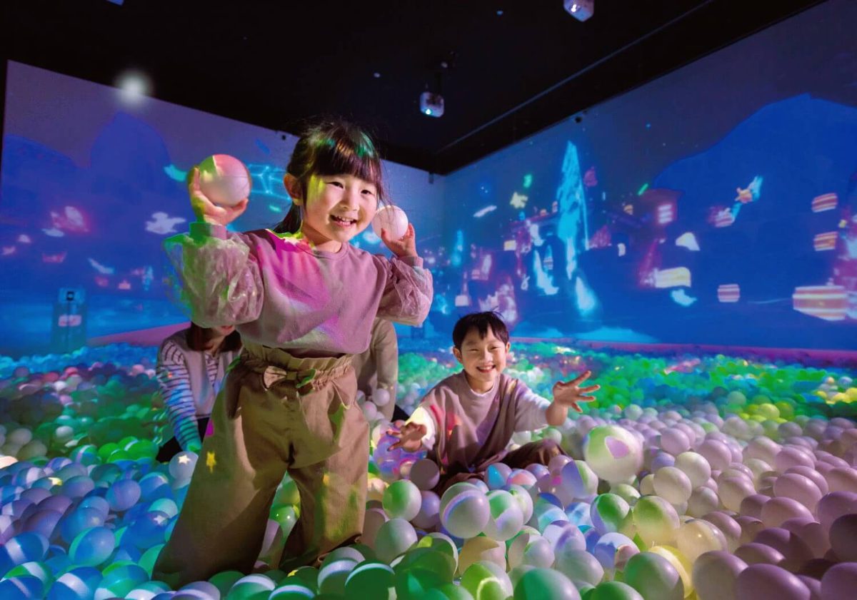 カラフルなボールが敷き詰められたプールで、壁と床に映像が映る中を子どもたちが遊んでいる