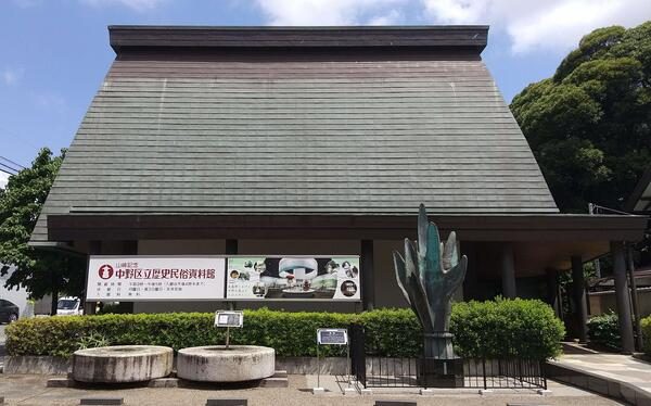中野区立歴史民俗資料館の外観。大きな屋根の建物の前に館名の看板と石臼
