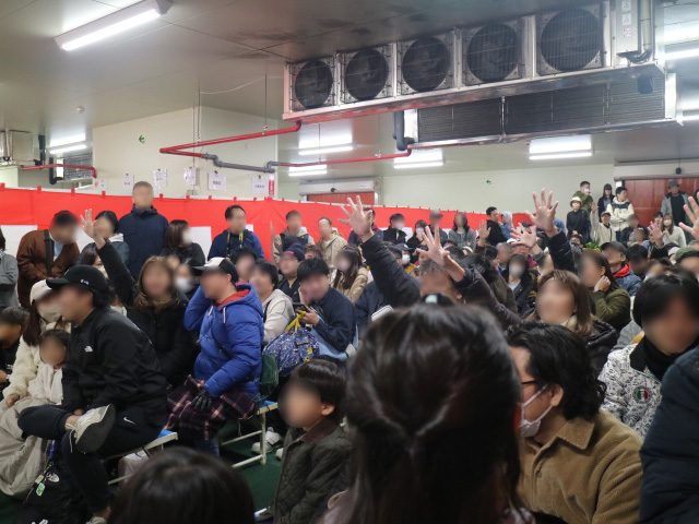 天井に冷却装置が並ぶ売場で、大勢の来場者が手を挙げて解体されたマグロの購入を申し出ている