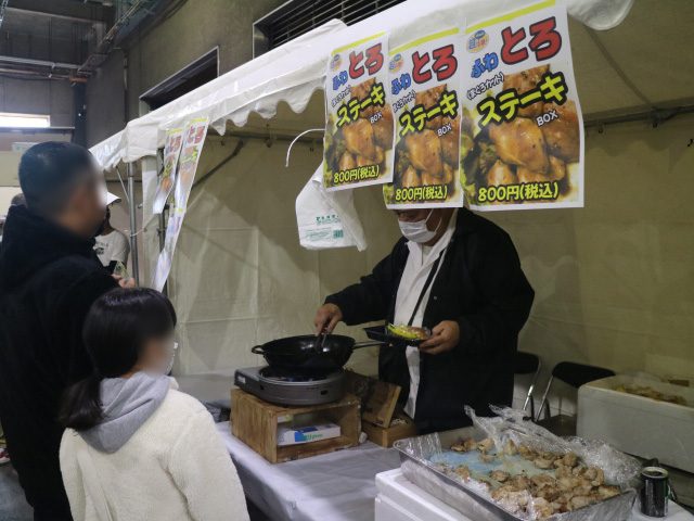 テントの屋台で「ねぎとろステーキ 800円(税込)」の貼り紙の前、店の人がフライパンで調理している