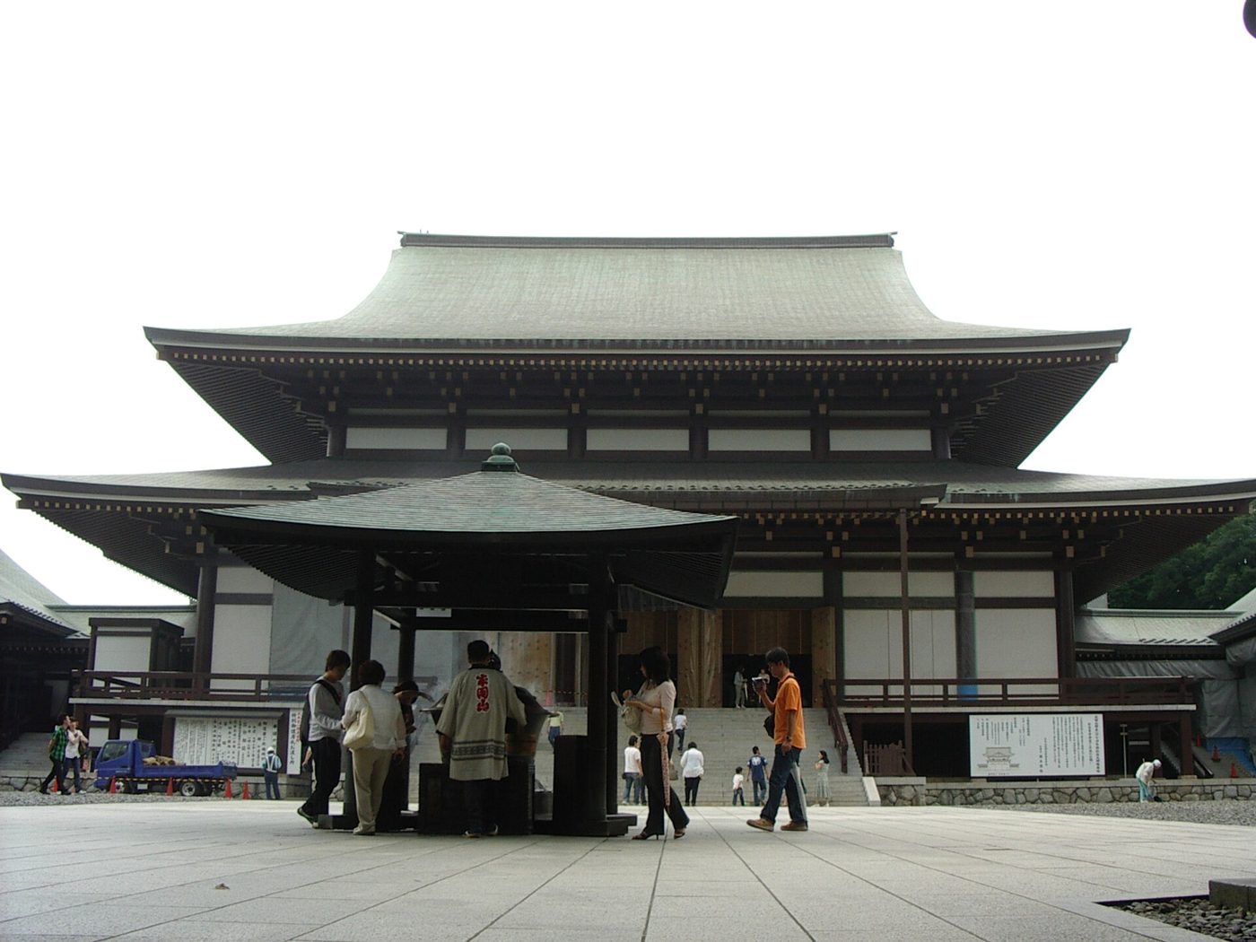 緑青色の大屋根の成田山新勝寺大本堂と、その手前に立つ屋根付きの香炉、周りを歩く参拝者