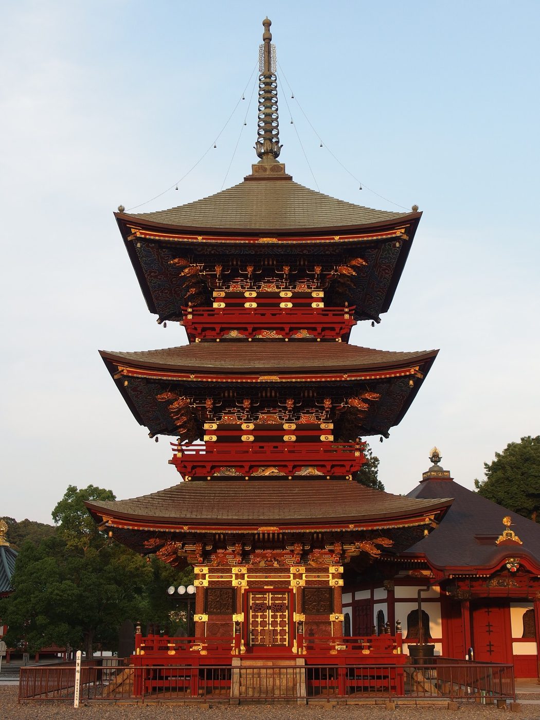 朱塗りの柱と極彩色の彫刻で飾られた成田山新勝寺の三重塔を正面から見上げた写真