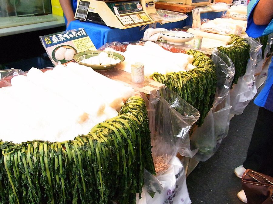 露店の台の上で、葉を付けたままの大根のべったら漬けが樽に山盛りに並び、はかりが置かれている様子