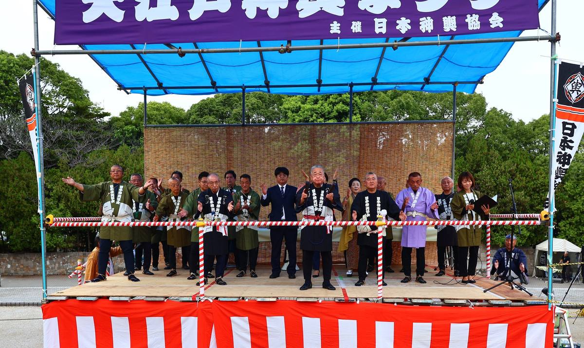 2025年の大江戸神輿まつりで、木場公園の石畳の広場に色とりどりの半纏を着た担ぎ手が大勢集まり、奥に神輿と提灯、高層ビルが見える様子