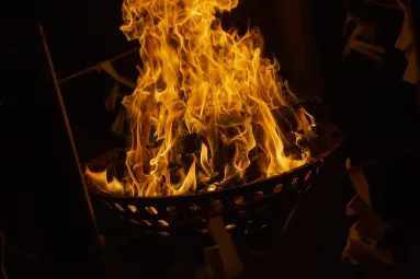 夜の境内で鉄のかごに組んだ薪が大きな炎を上げて燃えている、大湯祭のかがり火の写真
