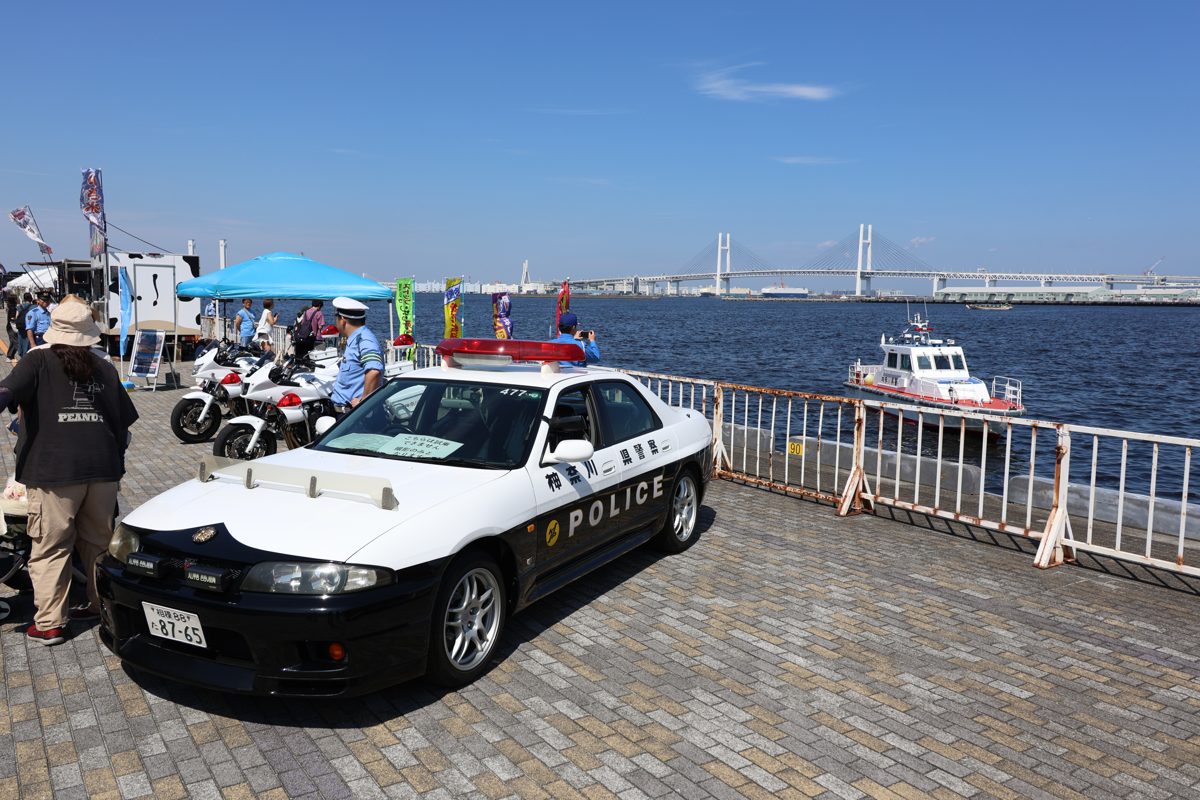 大さん橋の岸壁に展示されたパトカーと白バイ。背景に横浜ベイブリッジ。前年の大さん橋マルシェの車両展示