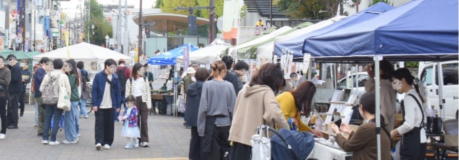 前回のおおたイチ推しマルシェの様子。大岡山駅前広場の歩道沿いに白と青のテントが並び、家族連れが買い物をしている