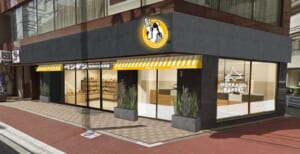 ペンギンベーカリー祖師ヶ谷大蔵店の外観イメージ。角地の黒い外壁の建物に黄色いひさしと「ペンギン」の看板