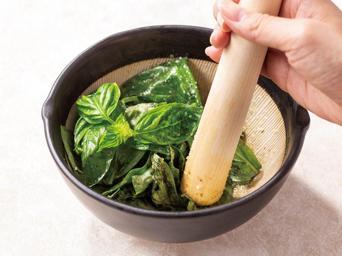 すり鉢とすりこぎを使い、生のバジルを擦ってソースを作る場面
