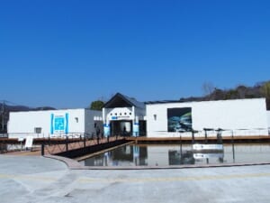 青空の下、水路の上に建つ白い平屋の建物と入口へ続く橋