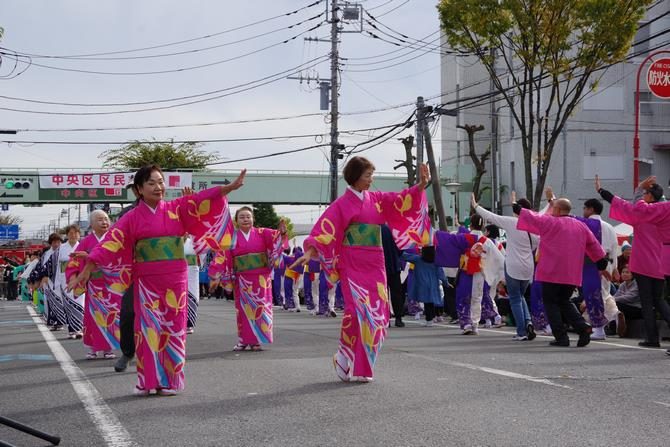 中央通りでピンクの浴衣の踊り手が列になって与野ふるさと音頭を踊っている。奥に中央区区民まつりの横断幕