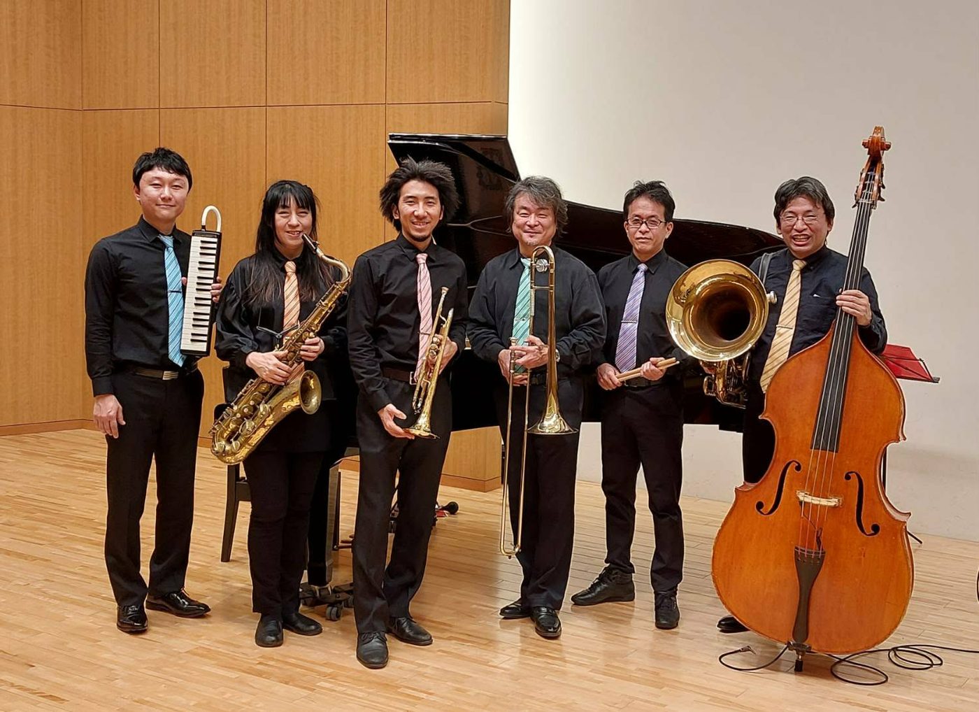 ステージに並ぶJOY SWING COMPANYの6人。鍵盤ハーモニカ、サックス、トランペット、トロンボーン、チューバ、ウッドベースを持つ