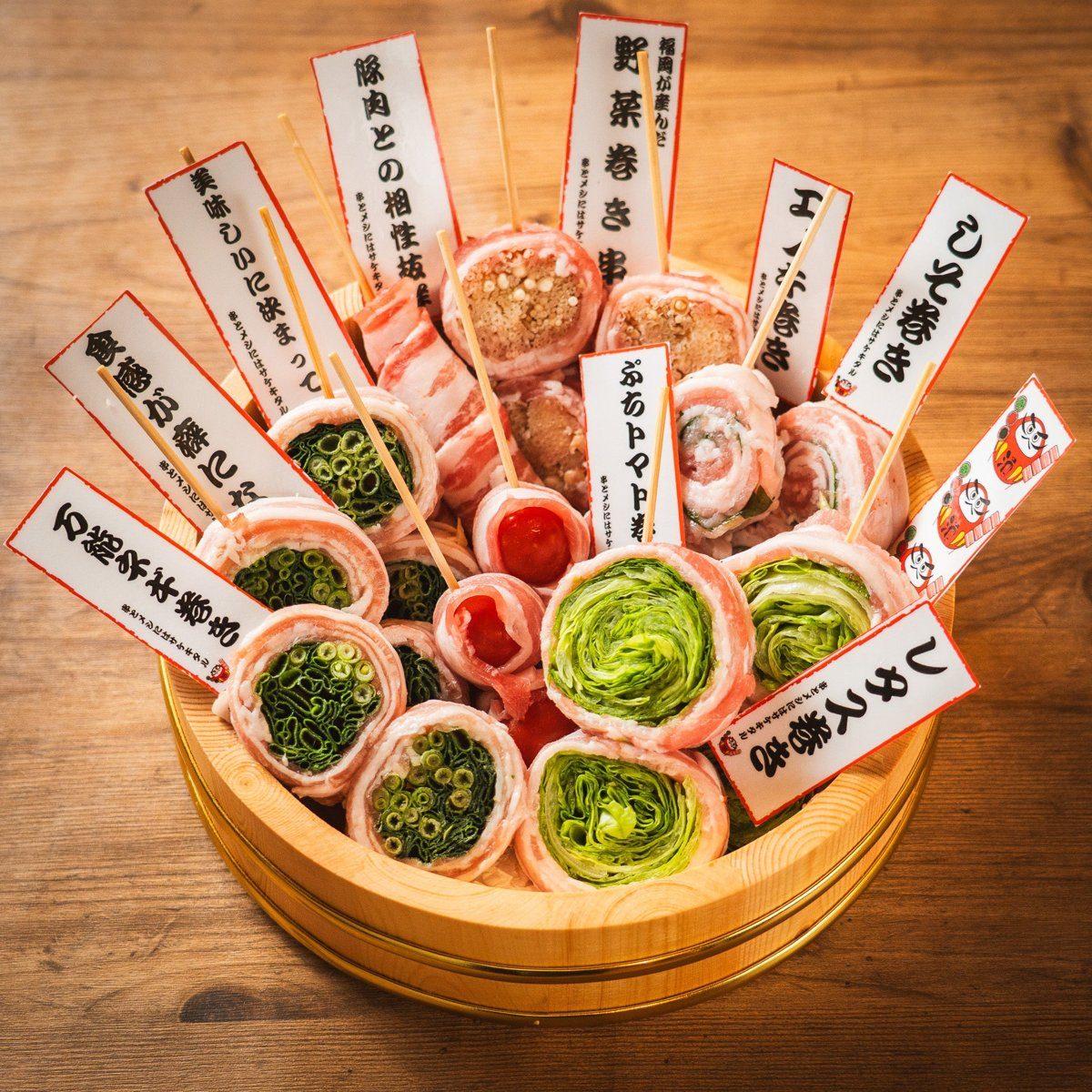 木の桶に、豚バラで巻いた野菜巻き串がたくさん立てて盛られ、レタス巻きなどの名札が刺さっている