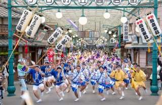 昭和の街並みを再現した夕日の丘商店街のアーケードの下を、青や黄色の浴衣の踊り手が提灯を掲げて流し踊りをしている様子