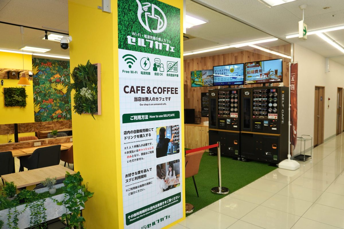 セルフカフェ フィールズ南柏店の入口。柱に「当店は無人のカフェです」と利用方法の案内板があり、奥にドリンクの自動販売機が並ぶ