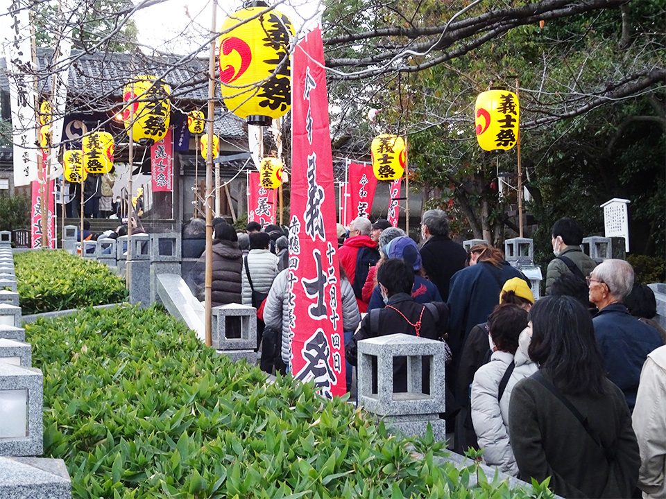 「義士祭」と書かれた黄色い提灯と赤いのぼりが並ぶ泉岳寺の境内で、参拝者が列を作っている様子