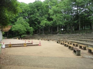 木立に囲まれた屋外の舞台と、その前に階段状に並ぶ客席とベンチ