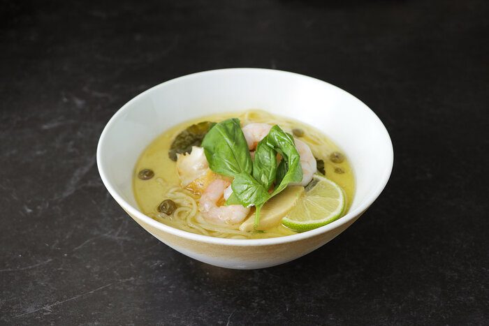 白い丼の緑色のスープに、バジル、海老、ライムがのった麺