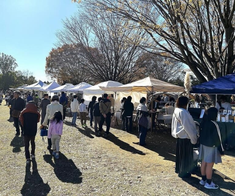 晴れた芝生の広場に白いテントが一列に並び、大勢の来場者が店を見て歩いている写真