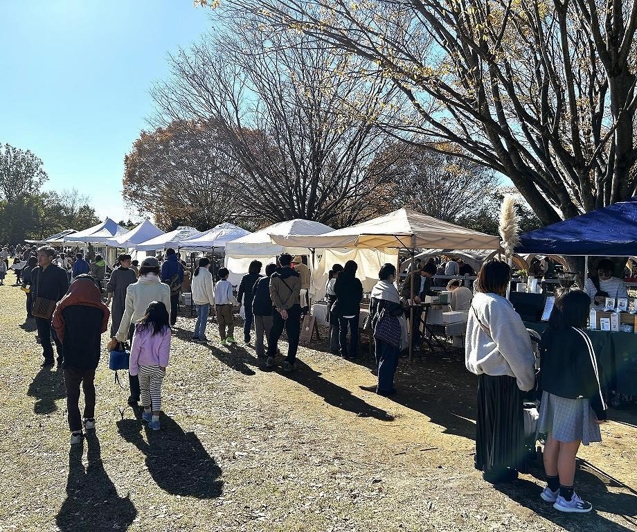 晴れた芝生の広場に白いテントが一列に並び、大勢の来場者が店を見て歩いている写真