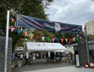 武蔵大学の正門に「第73回 武蔵大学 白雉祭 11.1 11.2」の横断幕と三角旗が飾られ、白いテントの受付に来場者が集まる様子