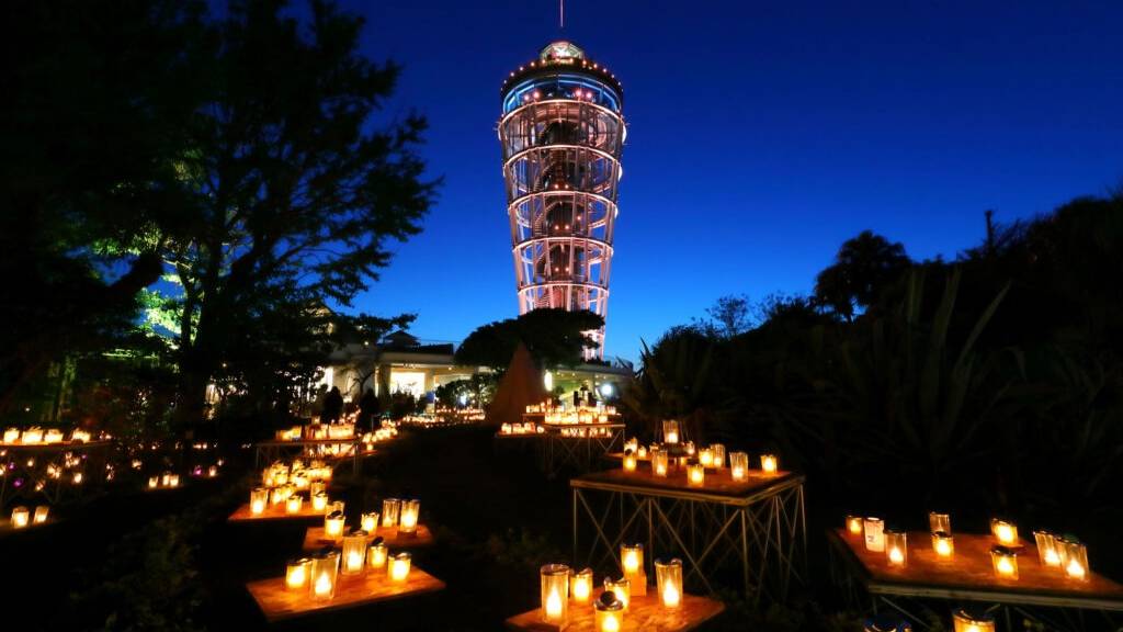 夜の江の島サムエル・コッキング苑。並んだキャンドルの奥にライトアップされた江の島シーキャンドル