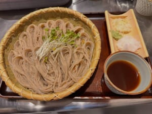 竹ざるに盛った細切りの蕎麦にかいわれ大根がのり、横に竹の器の薬味（大根おろし・わさび・ねぎ）と、つゆの入った器