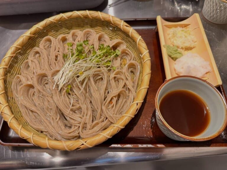 竹ざるに盛った細切りの蕎麦にかいわれ大根がのり、横に竹の器の薬味（大根おろし・わさび・ねぎ）と、つゆの入った器
