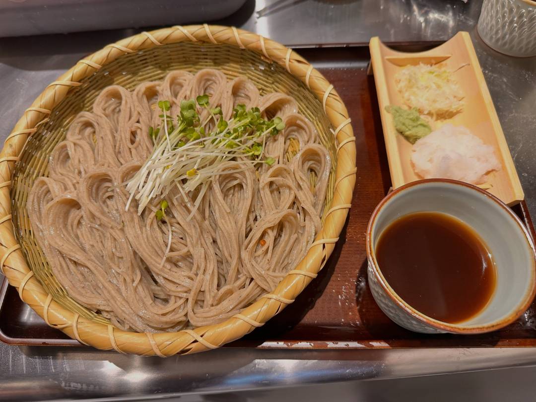 竹ざるに盛った細切りの蕎麦にかいわれ大根がのり、横に竹の器の薬味(大根おろし・わさび・ねぎ)と、つゆの入った器
