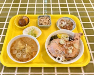黄色のトレーに骨付き鶏もも肉の鶏肉飯、ワンタンスープ、小鉢2品、漬物がのった昼のセット