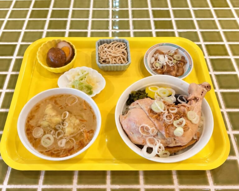 黄色のトレーに骨付き鶏もも肉の鶏肉飯、ワンタンスープ、小鉢2品、漬物がのった昼のセット