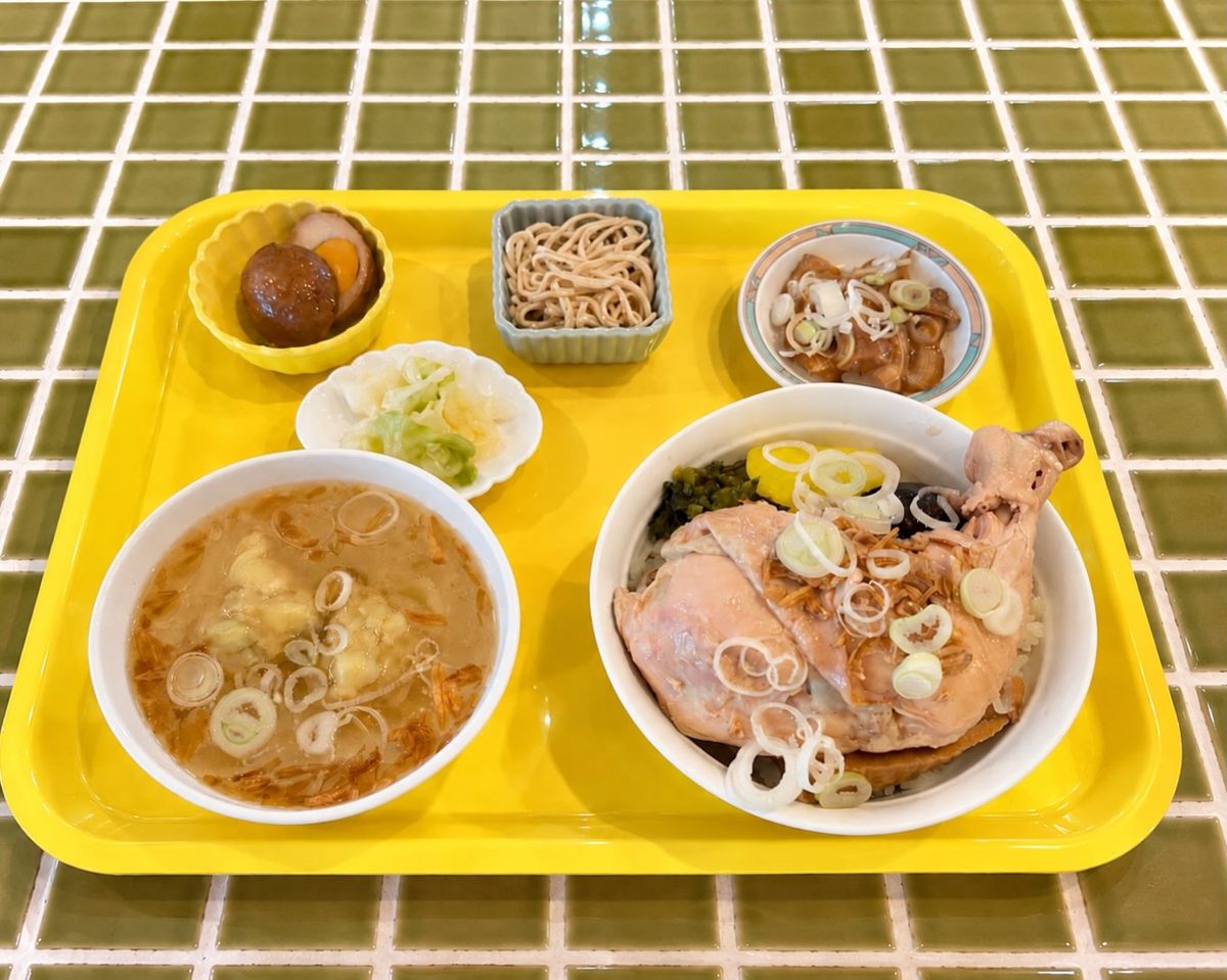 黄色のトレーに骨付き鶏もも肉の鶏肉飯、ワンタンスープ、小鉢2品、漬物がのった昼のセット