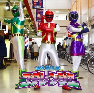 緑・赤・紫のスーツを着た地域宣伝隊コダレンジャーの3人が商店街でポーズをとる写真